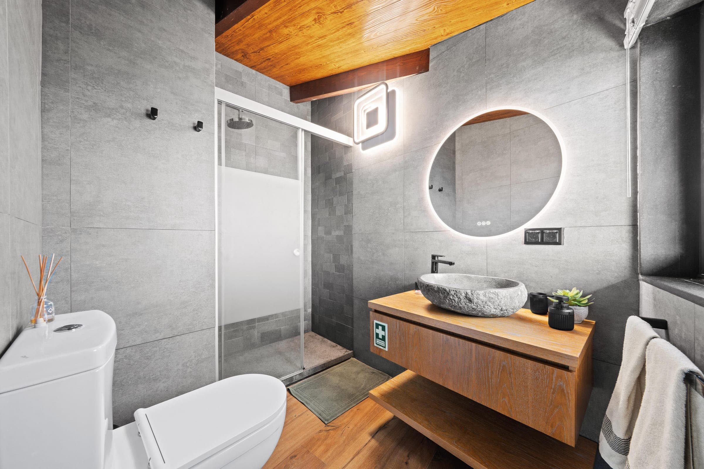 A natural-stone vessel basin beneath a round backlit mirror.
