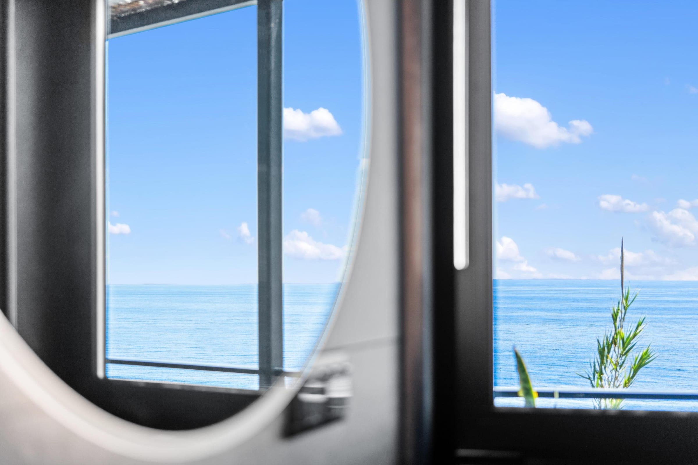 Reflections of sea and sky across the bathroom's glass and mirror.