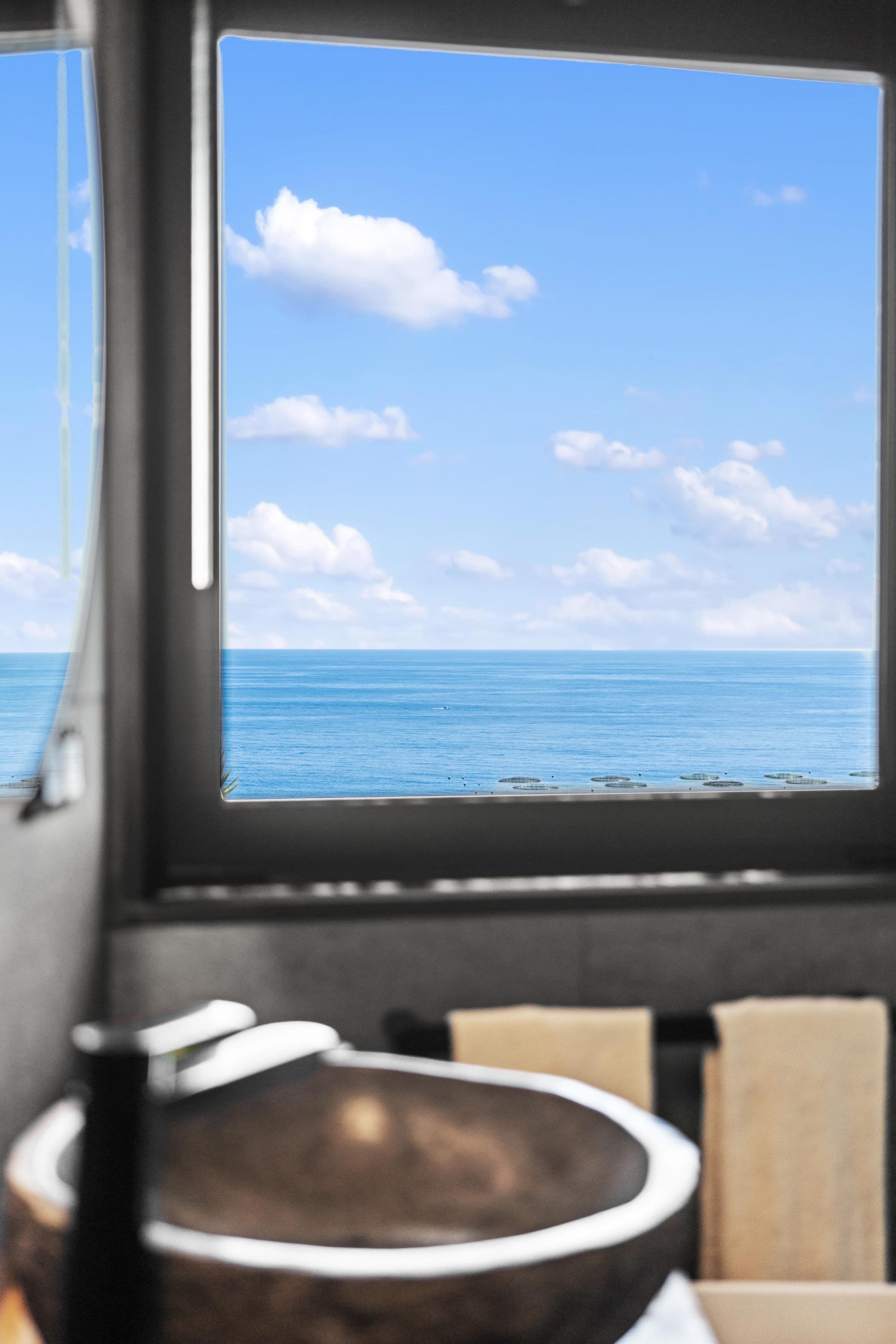 A stone basin catches the light beneath a wide sea-facing window.