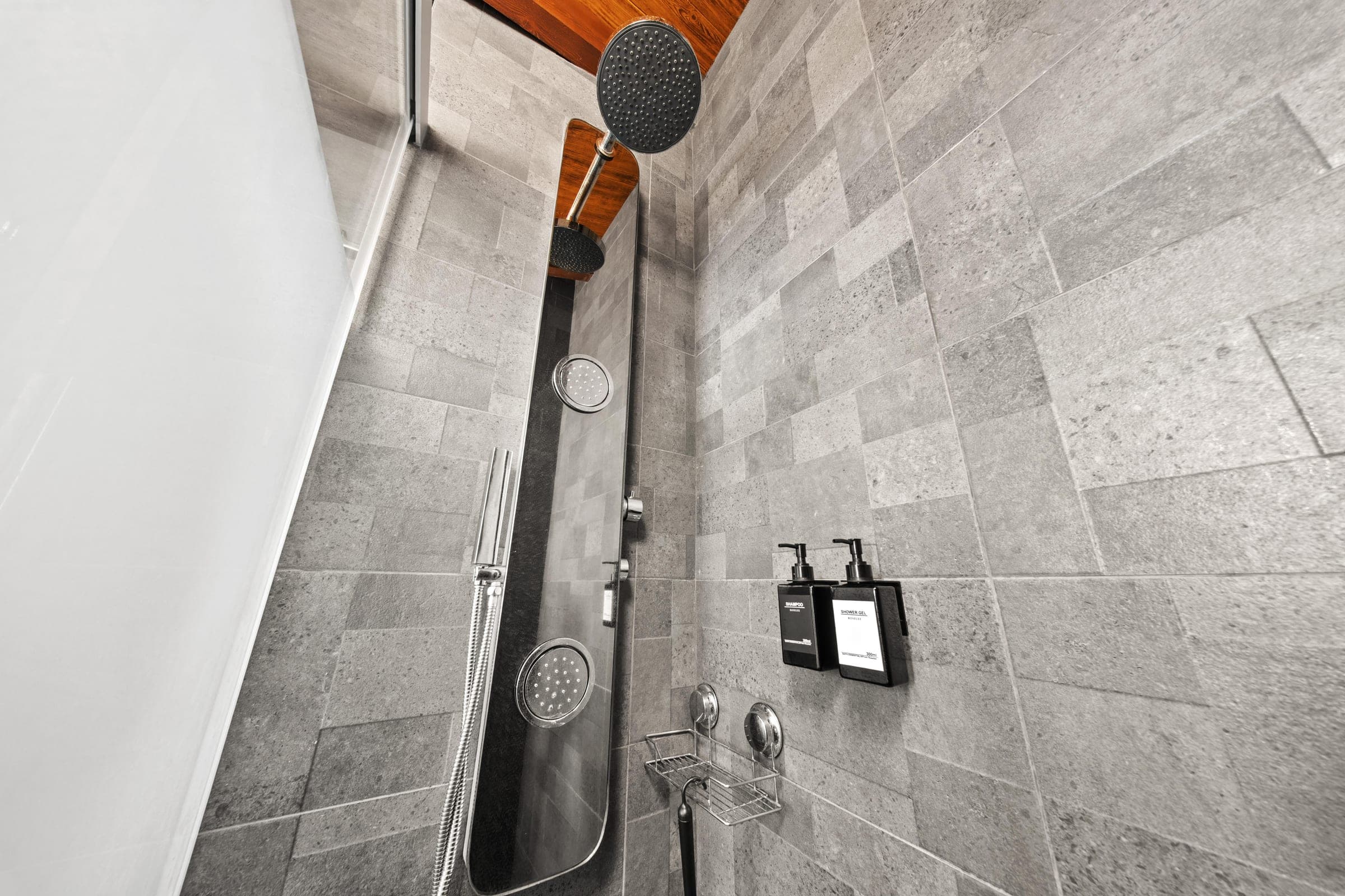 Rainfall shower head against warm wood beams and grey stone tile.