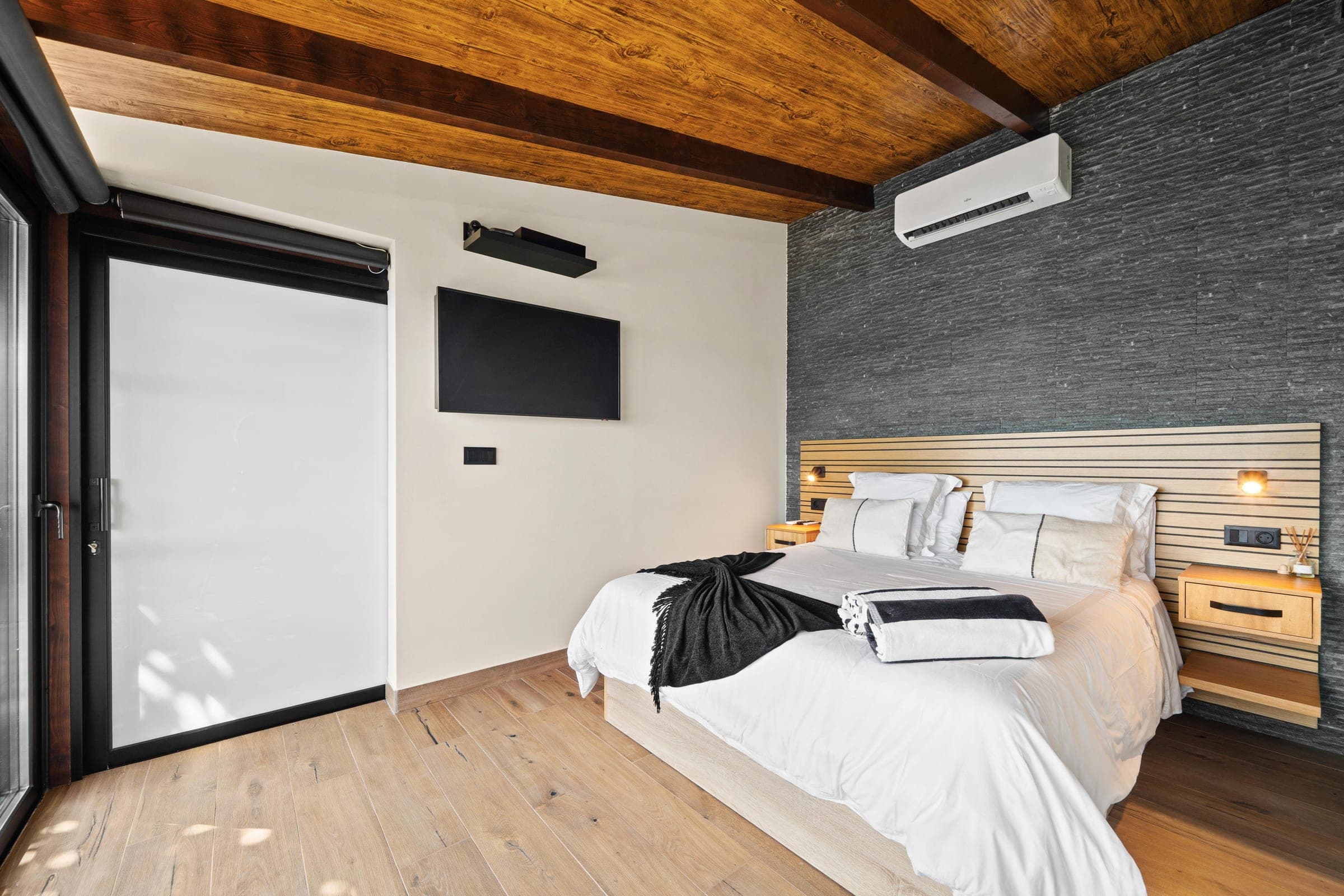 Bedroom with a dark stone accent wall and a slatted oak headboard.